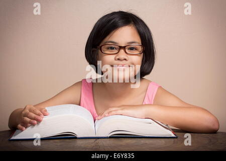 Jeune fille portant des lunettes la lecture à la maison Banque D'Images