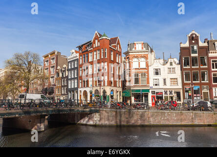 AMSTERDAM, Pays-Bas - 19 mars 2014 : maisons colorées le long de la berge du canal au printemps journée ensoleillée. Les gens ordinaires à pied Banque D'Images