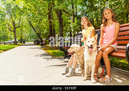 Deux jeunes filles avec des chiens assis dans un parc sur un banc Banque D'Images