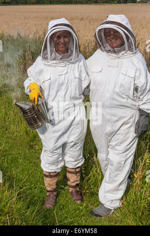 Les apiculteurs deux femmes vêtues de vêtements protecteurs, prêt à travailler sur leurs ruches. L'un est titulaire d'un fumeur. Banque D'Images