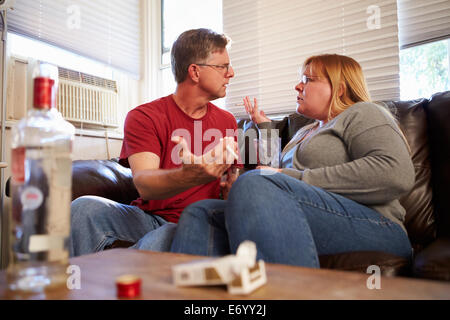 Couple Arguing On Sofa avec bouteille de vodka et de cigarettes Banque D'Images