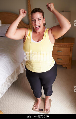 Surpoids femme pesant elle-même à des échelles dans la chambre Banque D'Images