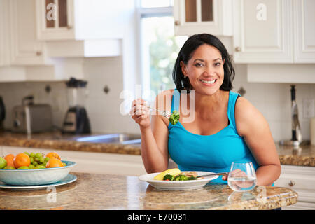 L'excès de Woman Eating Healthy meal in Kitchen Banque D'Images