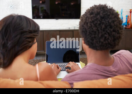 Vue arrière du couple Sitting on Sofa Using Laptop Banque D'Images