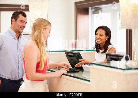 Couple de l'enregistrement à la réception de l'hôtel Using Digital Tablet Banque D'Images