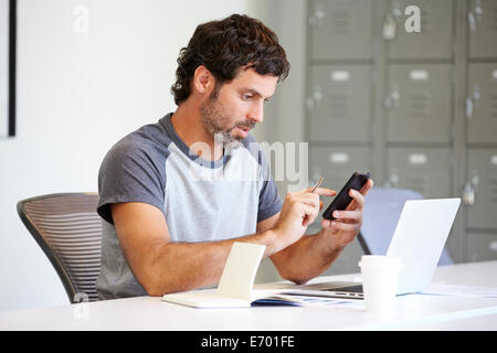 L'homme habillé en passant à l'aide de Mobile Phone In Design Studio Banque D'Images