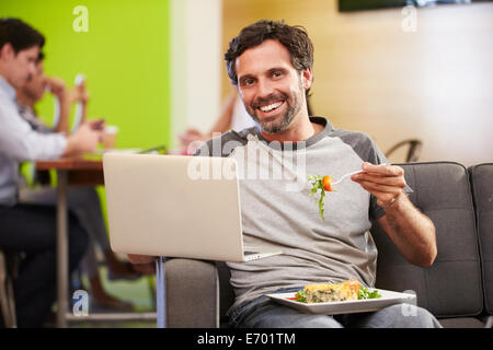 Homme assis sur un canapé et manger le déjeuner In Design Studio Banque D'Images