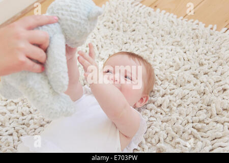 Femme hand holding up ours pour baby girl lying on rug Banque D'Images