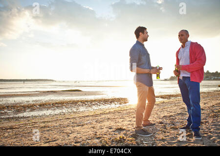 Les hommes de boire une bière et de discuter sur la plage Banque D'Images