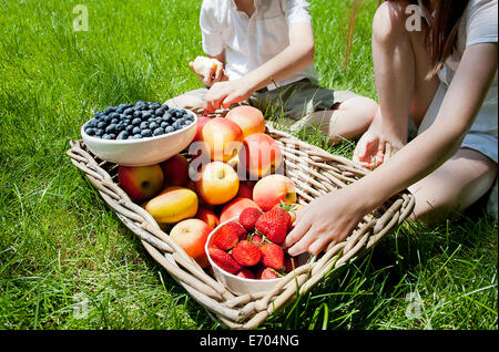 Portrait de frère et soeurs en mangeant des fruits de panier sur l'herbe Banque D'Images