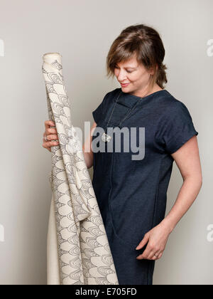 Studio portrait of mature female fashion designer holding up a roll of textile Banque D'Images