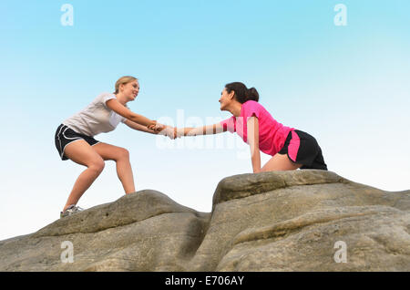 Young female runner aider ami vers le haut de rock formation Banque D'Images