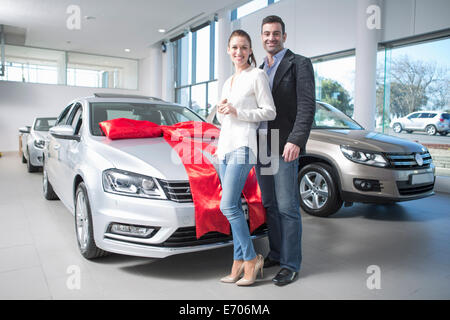 Portrait of mid adult couple et nouvelle voiture avec arc rouge dans l'agence de voiture Banque D'Images