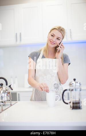 Young woman chatting on smartphone et en remuant le café dans la cuisine Banque D'Images