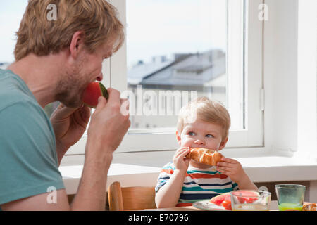 Le père et le petit garçon qui mange son petit-déjeuner à table de cuisine Banque D'Images