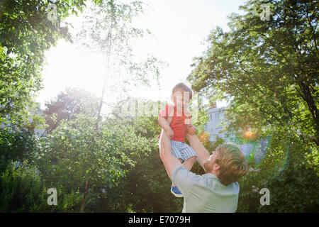 Père holding up toddler son in park Banque D'Images