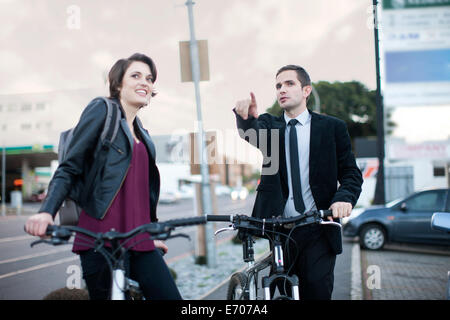 Jeune femme prenant itinéraire de l'homme d'affaires tandis que le vélo en ville Banque D'Images