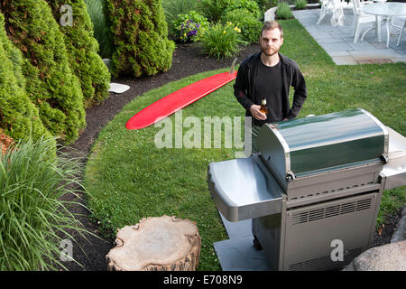 Portrait of mid adult man standing by barbecue avec bouteille de bière dans le jardin Banque D'Images