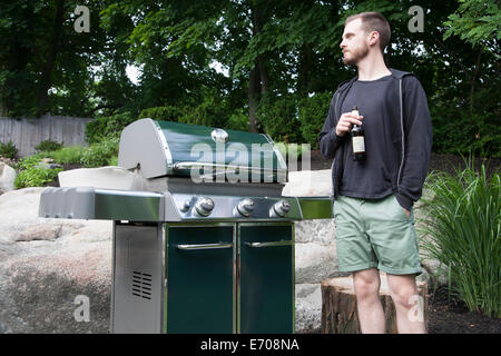 Mid adult man standing by barbecue avec bouteille de bière dans le jardin Banque D'Images