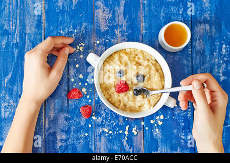 Vue du dessus montrant les mains manger du gruau aux fruits rouges un miel, sur une table en bois bleu Banque D'Images