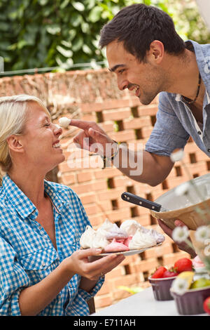 Jeune couple de jouer avec de la meringue at garden party Banque D'Images