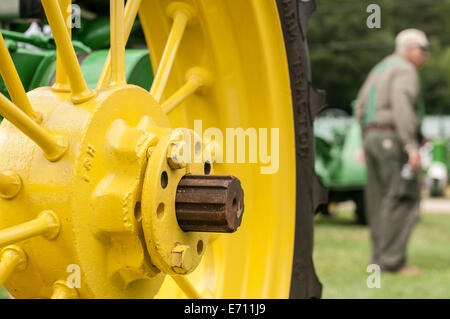 Un agriculteur passe devant l'emblématique des roues du tracteur John Deere jaune à un tracteur John Deere Expo de New Hampshire, USA. Banque D'Images