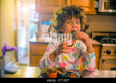 Portrait de surprise girl eating cupcakes au comptoir de la cuisine Banque D'Images