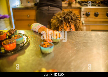 Portrait of Girl Reaching for cupcakes au comptoir de la cuisine Banque D'Images