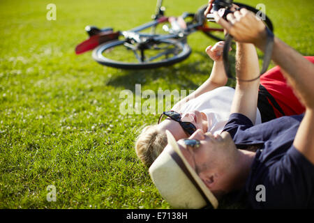 Couple lying in park looking at photographs sur appareil photo numérique Banque D'Images