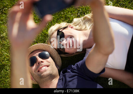 Couple lying in park en tenant sur smartphone selfies Banque D'Images