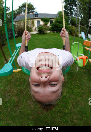 Enfant sur une balançoire se balancer la tête en bas Banque D'Images