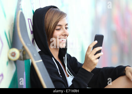 Jeunes patineurs happy teen girl en utilisant un téléphone intelligent avec un mur de graffiti flou en arrière-plan Banque D'Images