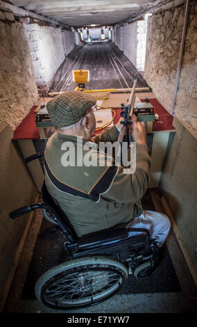 Un fauteuil roulant à l'aide de cadre supérieur retraité homme handicapé de charger son fusil à air à un club de tir éventail UK Banque D'Images