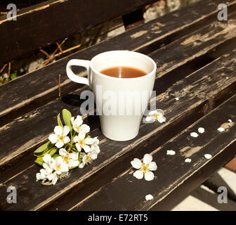 White tasse de café ou de chocolat chaud sur un banc marron avec des fleurs blanches. Banque D'Images