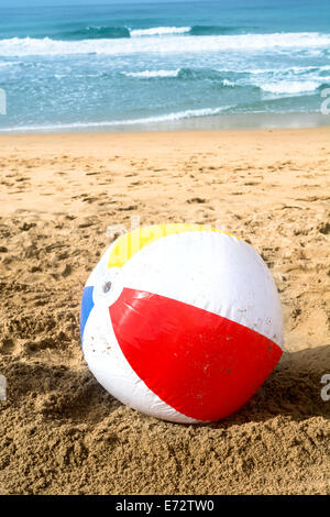Un ballon de plage en été, se lave jusqu'à la plage de sable tandis qu'un océan turquoise gronde paisiblement dans l'arrière-plan. Banque D'Images