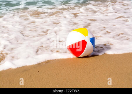 Un ballon de plage en été, se lave jusqu'à une plage de sable pendant qu'elle était poussée par les océans, douce mousse surf. Banque D'Images