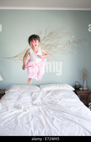 Girl (6-7) jumping on bed with lollipops dans la main Banque D'Images