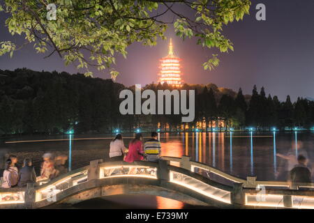 La Pagode Leifeng avec visiteurs assis sur les rails d'un pont en arc de pierre éclairé au lac de l'Ouest, à Hangzhou, Zhejiang, Chine Banque D'Images