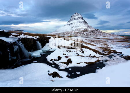 Kirkjufell recouvert de neige avec une rivière gelée et cascade au premier plan, Grundarfjordur, Péninsule de Snæfellsnes, l'Islande Banque D'Images