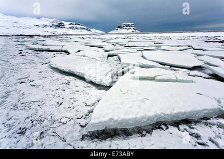 Vue sur plaques de glace de lac cassé couvert de neige en direction de Kirkjufell, près de Grundarfjordur, Péninsule de Snæfellsnes, l'Islande Banque D'Images