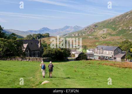 Vue de petit village avec des promeneurs marchant sur la colline et Snowdon horseshoe lointaines montagnes à la fin de l'été. Capel Curig North Wales Royaume-uni Grande-Bretagne Banque D'Images