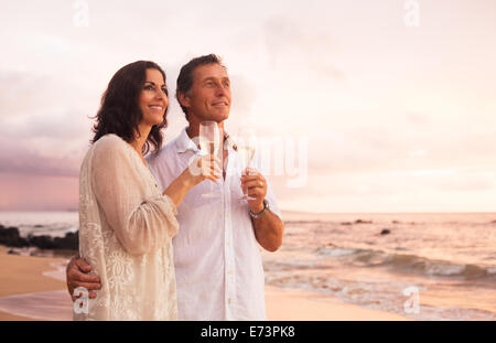 Happy Mature Couple Drinking Champagne sur la plage au coucher du soleil. La retraite de voyages vacances anniversaire. Banque D'Images