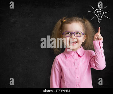 Happy kid girl à verres à l'idée lumineuse, debout près de l'école tableau noir en classe Banque D'Images