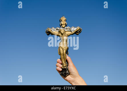 Symbole du christianisme metal croix avec le Christ crucifié dans femme Main sur fond de ciel bleu Banque D'Images