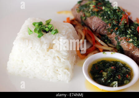 Viande avec chimichurri servi sur un lit de légumes et riz blanc dans un restaurant. Banque D'Images
