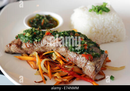 Viande avec chimichurri servi sur un lit de légumes et riz blanc dans un restaurant. Banque D'Images