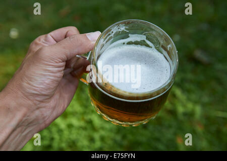 Tenir la main verre de bière blonde avec green lawn grass background, Cheers ! Banque D'Images