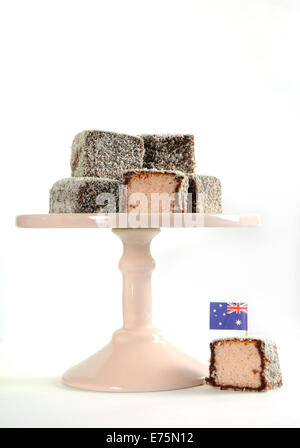 Gâteau traditionnel Australien, Lamington, rose pâle sur cake stand contre un fond blanc. Banque D'Images