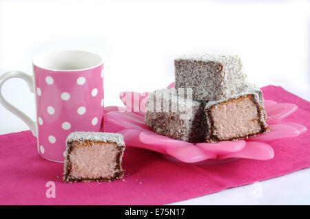 Gâteau traditionnel Australien, Lamington, sur plaque rose et blanc à pois rose avec serviette tasse de café sur un fond blanc. Banque D'Images