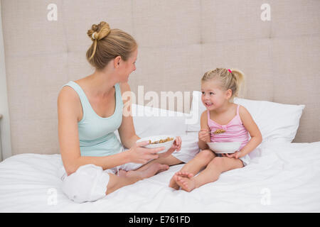 Cute little girl et mère sur bed eating cereal Banque D'Images